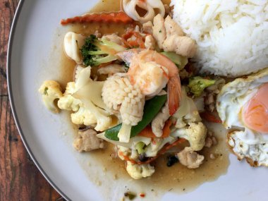 Kızarmış sebze, karnabahar, havuç, pirinç ve ahşap arka plan üzerinde beyaz tabak içinde kızarmış yumurta ile deniz ürünleri ile şeker bezelye karışımı. Tay tarzında gıda.