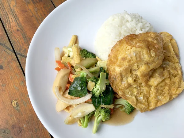 Ahşap arka plan beyaz bir tabağa omlet ile kızartma sebze ilave edin. Tay tarzı yiyecek. Vejetaryen yiyecekler