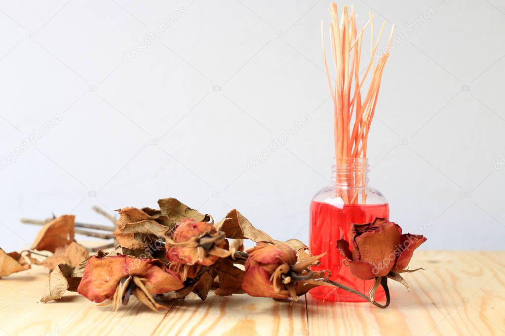 Hand made pf Fragrance Diffuser Set: bottle with aroma sticks and dry red rose, a spray bottle with perfume on pine wood table with wall background.