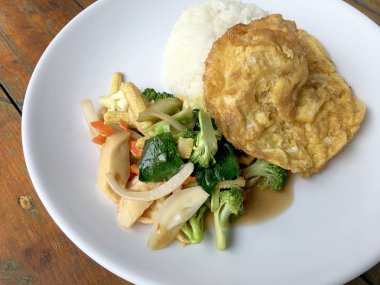 Ahşap arka plan beyaz bir tabağa omlet ile kızartma sebze ilave edin. Tay tarzı yiyecek. Vejetaryen yiyecekler