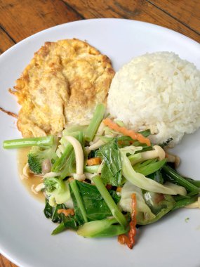 Kızarmış sebze Tay omlet (yumurta) ile pirinç rustik ahşap arka plan üzerinde beyaz plaka ile karıştırın. Vejetaryen yiyecekler, sağlıklı gıda.