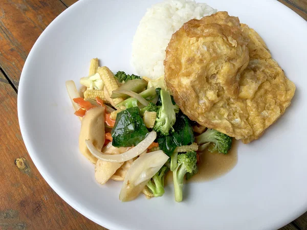 Ahşap arka plan beyaz bir tabağa omlet ile kızartma sebze ilave edin. Tay tarzı yiyecek. Vejetaryen yiyecekler