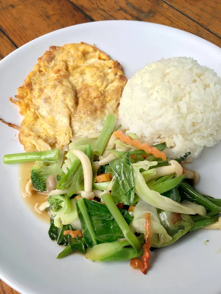 Kızarmış sebze Tay omlet (yumurta) ile pirinç rustik ahşap arka plan üzerinde beyaz plaka ile karıştırın. Vejetaryen yiyecekler, sağlıklı gıda.