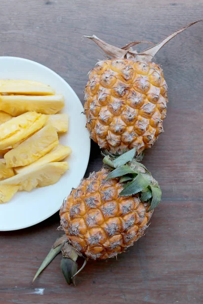Taze kesme ananas ve ananas kabuklu Asya tarzı eski ahşap arka plan üzerinde beyaz tabak içinde. Tropikal meyve kavramı.