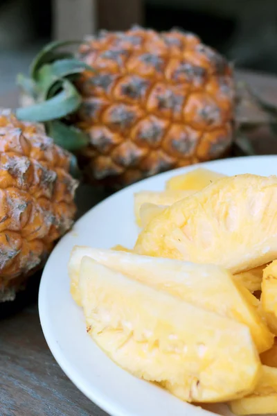 Cutting fresh pineapple and pineapple shelled Asian-style in white dish on the old wooden background. Tropical fruit concept.