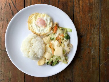 Tofu ve ahşap arka plan üzerinde beyaz tabak pirinç kızarmış yumurta ile tavada kızartılmış karışık sebze. Vejetaryen yiyecekler, sağlıklı gıda.