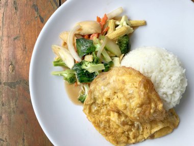 Ahşap arka plan beyaz bir tabağa omlet ile kızartma sebze ilave edin. Tay tarzı yiyecek. Vejetaryen yiyecekler