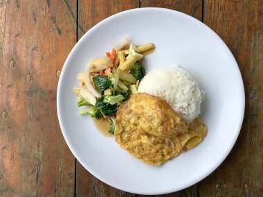 Ahşap arka plan beyaz bir tabağa omlet ile kızartma sebze ilave edin. Tay tarzı yiyecek. Vejetaryen yiyecekler