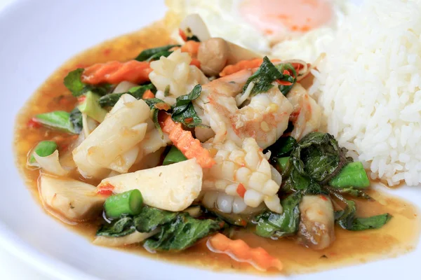 Asya gıda, kızarmış heyecan chili Yapıştır ile deniz ürünleri ve pirinç beyaz tabakta, baharatlı sıcak biber Tayland yemekleri ile fesleğen yaprakları.