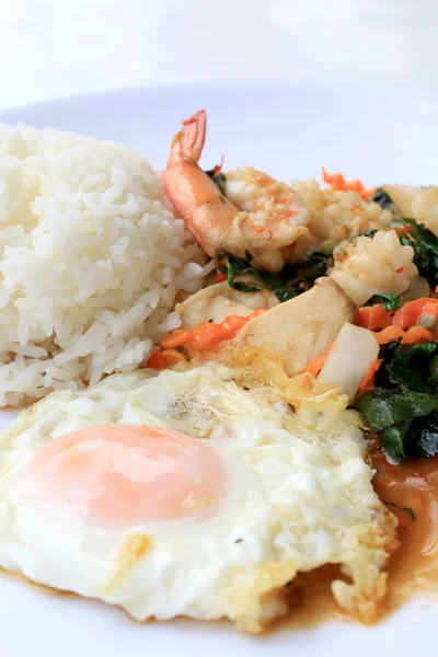 Asya gıda, kızarmış heyecan chili Yapıştır ile deniz ürünleri ve pirinç beyaz tabakta, baharatlı sıcak biber Tayland yemekleri ile fesleğen yaprakları.