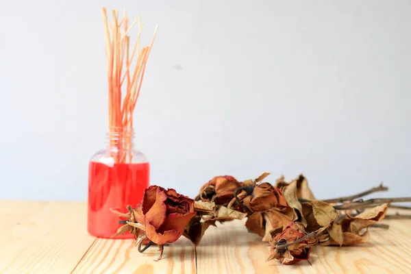 El yapımı pf koku difüzör ayarla: şişe aroma sopalarla ve kuru kırmızı gül (reed difüzör), çam ahşap masa duvar arka plan ile parfüm sprey şişeyle.
