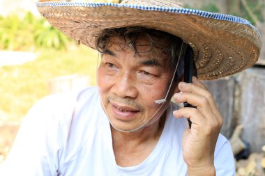 Tayland 'ın kuzeyinde ters dönmüş havza şeklinde bambudan yapılmış şapkası ve palmiye yaprakları olan kıdemli Asyalı adam telefonda bahçedeki işiyle ilgili konuşuyor.