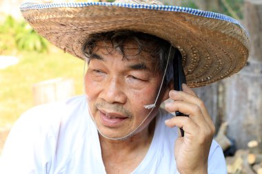 Tayland 'ın kuzeyinde ters dönmüş havza şeklinde bambudan yapılmış şapkası ve palmiye yaprakları olan kıdemli Asyalı adam telefonda bahçedeki işiyle ilgili konuşuyor.