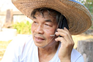Tayland 'ın kuzeyinde ters dönmüş havza şeklinde bambudan yapılmış şapkası ve palmiye yaprakları olan kıdemli Asyalı adam telefonda bahçedeki işiyle ilgili konuşuyor.