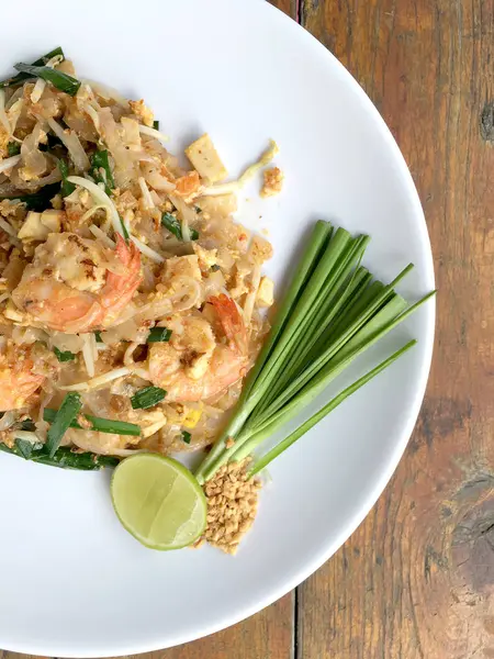 Пад Тай, жареная рисовая лапша с креветками в белой тарелке на деревянном столе. Одно из главных блюд Таиланда. популярная еда в Таиланде. Тайский жареный лапша — стоковое фото