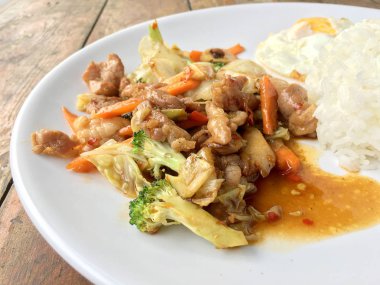 Tayland baharatlı yemekleri: bir tabak domuz stir fry ile sebze ve pirinç ahşap masa üzerinde beyaz tabak kızarmış yumurta. sağlıklı yemek.