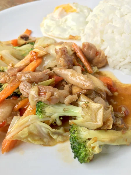 Makanan pedas Thailand: sepiring daging babi goreng dengan sayuran dan telur goreng dengan nasi dalam hidangan putih di atas meja kayu. hidangan sehat . — Stok Foto