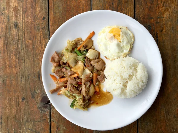 Thai spicy food : A plate of pork stir fry with vegetables and fried egg with rice in white dish on wooden table.  healthy dish. — Stock Photo, Image