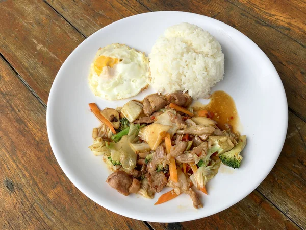 Tayland baharatlı yemekleri: bir tabak domuz stir fry ile sebze ve pirinç ahşap masa üzerinde beyaz tabak kızarmış yumurta. sağlıklı yemek.
