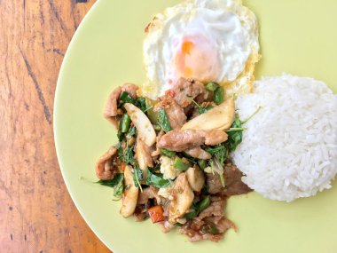 Tayland baharatlı yemekleri fesleğen domuz kızarmış pilav tarifi (Krapao Gai) ahşap zemin üzerine yeşil plaka kızarmış yumurta ile. Tayland gıda.