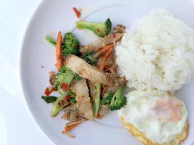 Kavrulmuş Chili Yapıştır ve karışık sebze soslu kızarmış gevrek domuz eti ilave edin; fesleğen; Kale; brokoli; havuç; kırmızı biber ve sahanda yumurta beyaz arka plan üzerinde beyaz tabak içinde Tayland Yasemin pirinç ile. Tay tarzında gıda.