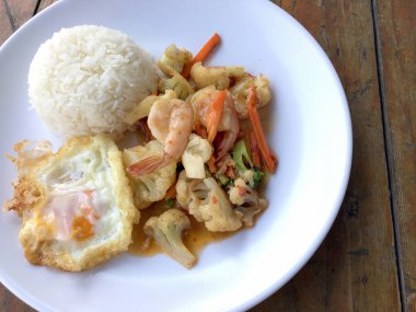 fasulye ve pilav ve kızarmış yumurta ahşap arka plan üzerinde beyaz tabak karides sebzeler ile tavada. Tay tarzında gıda.