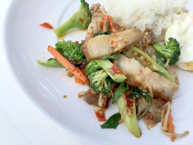 Kavrulmuş Chili Yapıştır ve karışık sebze soslu kızarmış gevrek domuz eti ilave edin; fesleğen; Kale; brokoli; havuç; kırmızı biber ve sahanda yumurta beyaz arka plan üzerinde beyaz tabak içinde Tayland Yasemin pirinç ile. Tay tarzında gıda.