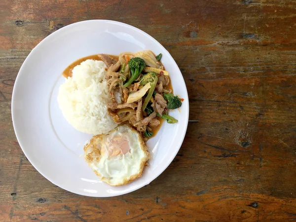 Asya tarzı tavada et dilimleri pilav ve kızarmış yumurta beyaz tabak ahşap masa üzerinde yerleştirilen Tay tarzında taze sebze ile.
