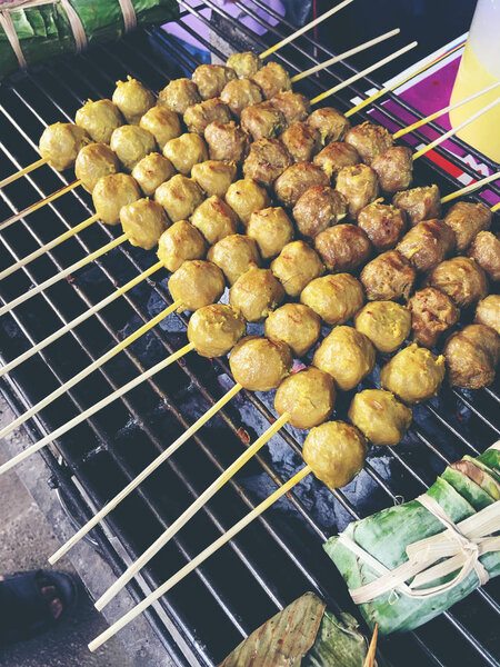 Thai meatballs on a grill on the steel stove on fire at the market. Thai street food. vintage tone.