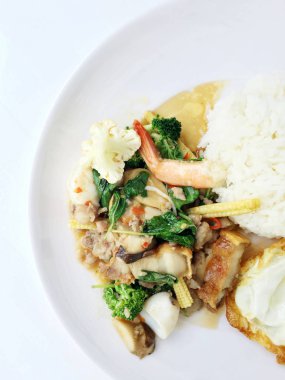 Kızarmış gevrek domuz eti ilave edin, karides, Tay kutsal fesleğen, chilies, sarımsak ve soya sosu ile deniz ürünleri karıştırın. kızarmış yumurta stil tepesi beyaz arka plan üzerinde beyaz tabak pirinç ve Tay dili ile.