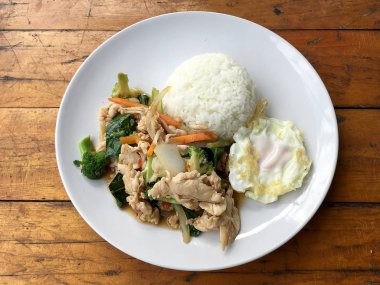 karışık sebze ve pirinç eski ahşap masa üzerinde beyaz tabak içinde Tay tarzında kızarmış yumurta ile tavada kızartılmış tavuk. Asya Tayland gıda.