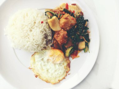 Baharatlı karıştırın kızarmış balık fileto pirinç ve beyaz arka plan üzerinde beyaz tabak kızarmış yumurta ile Tay ot ile. Vintage rengi.