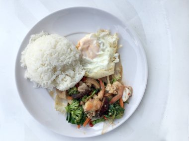 Tay gıda sağlıklı sebze kizartma tabak brokoli, mantar, havuç, hearb, kalamar ve pilav ve kızarmış yumurta beyaz arka plan üzerinde beyaz tabak karides tavada kızartılmış. Tay tarzında lokanta orde olabilir