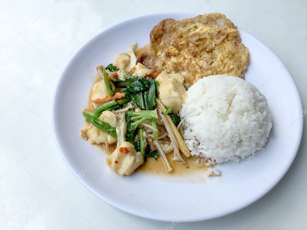 Stir vegetables with Tofu in chinese style with gravy Sauce and thai style omelet with rice in white plate on background. Vegetarian Food, healthy food.