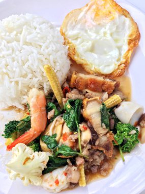 Kızarmış gevrek domuz eti ilave edin, karides, Tay kutsal fesleğen, chilies, sarımsak ve soya sosu ile deniz ürünleri karıştırın. kızarmış yumurta stil tepesi beyaz arka plan üzerinde beyaz tabak pirinç ve Tay dili ile.