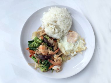 Tay gıda sağlıklı sebze kizartma tabak brokoli, mantar, havuç, hearb, kalamar ve pilav ve kızarmış yumurta beyaz arka plan üzerinde beyaz tabak karides tavada kızartılmış. Tay tarzında lokanta orde olabilir