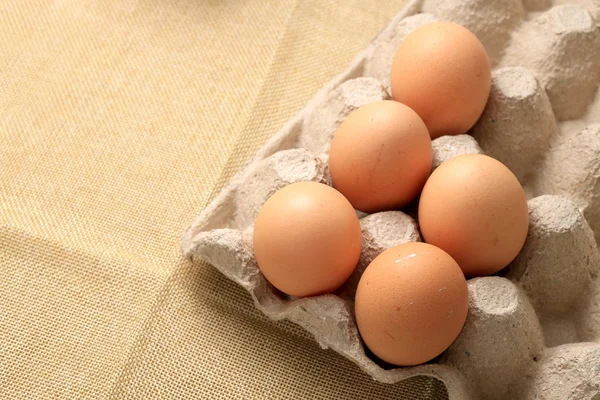 Fresh chicken eggs In the thirty box paper and have empty space for egg on cream fabric background.