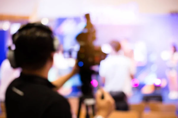 blurred image of young cameraman using a professional camcorder in door at event filming music show or mini concert for shooting some video movie and live broadcasting for online TV commercial