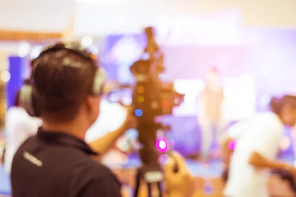 blurred image of young cameraman using a professional camcorder in door at event filming music show or mini concert for shooting some video movie and live broadcasting for online TV commercial