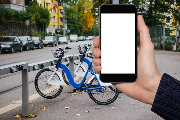 Hand with phone on a background of bicycle rental — Stock Photo, Image