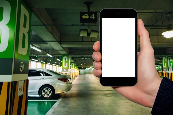 Hand with a smartphone on the background of car parking — Stock Photo, Image