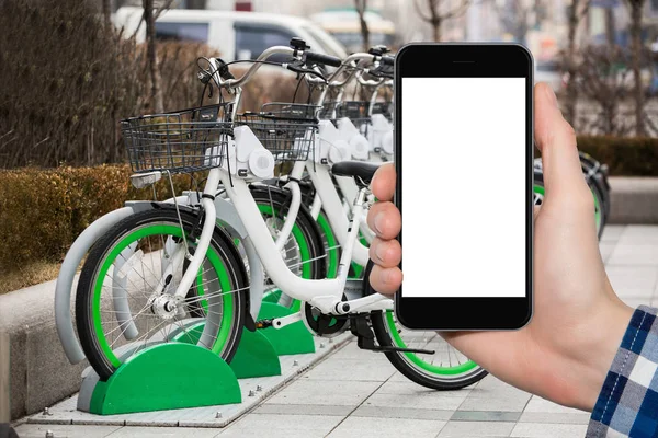 自転車レンタルの背景上で携帯電話を持つ手 — ストック写真
