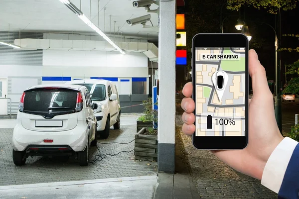 Handen met telefoon op een achtergrond van elektrische auto's opladen punt. — Stockfoto