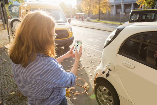 Γυναίκα με τηλέφωνο σε ένα φόντο από ηλεκτρικά αυτοκίνητα, φόρτιση σημείο. — Φωτογραφία Αρχείου