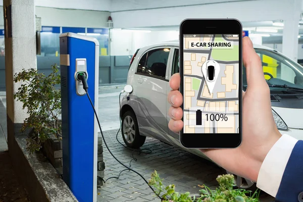 Handen met telefoon op een achtergrond van elektrische auto's opladen punt. — Stockfoto