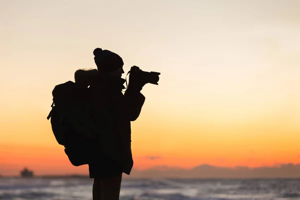 Мандрівник з рюкзаком стоїть на березі моря і фотографує схід сонця — стокове фото