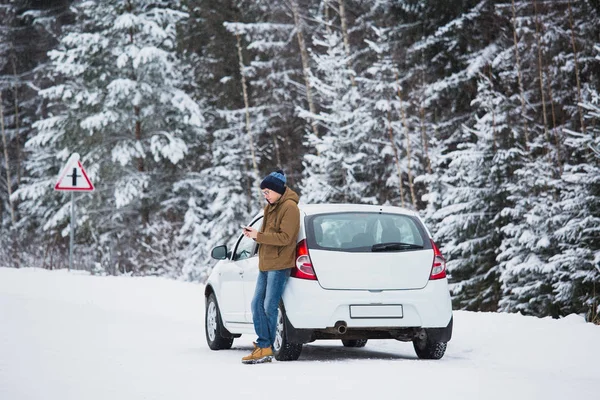 Giovane uomo è in piedi accanto alla macchina su una strada invernale . — Foto Stock