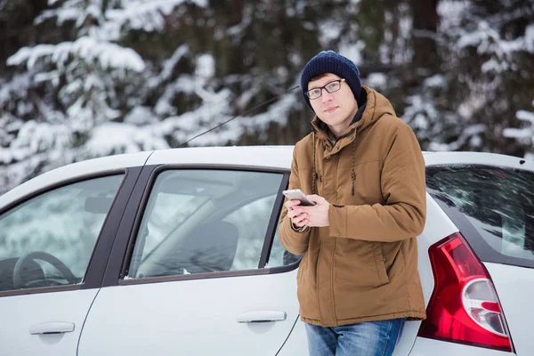 El joven está de pie junto al coche en una carretera de invierno. . — Foto de Stock