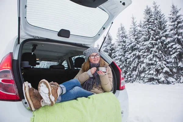 Jonge vrouw zit in de kofferbak van de auto en houdt een kop hete thee — Stockfoto