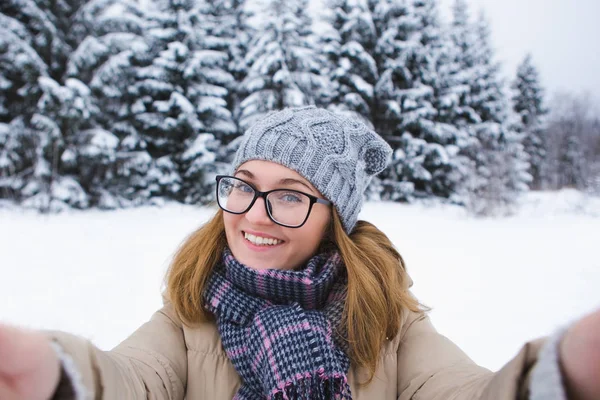 Jovem mulher leva selfie em um fundo de floresta de inverno coberta de neve. — Fotografia de Stock